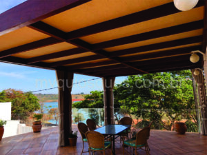 Um quiosque forrado com palhas, na cor castanho buclê com uma mesa e cadeiras logo abaixo.