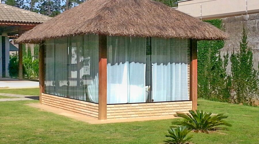 Quiosque com cobertura de sapê e fechamento com paredes e vidro.