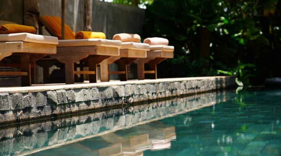 Uma Fileira De Cadeiras De Madeira Sentadas Ao Lado De Uma Piscina Y_bjlQYfQ_0