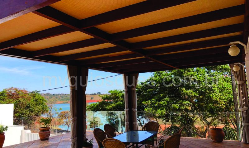 palha-castanho-buclê-com-marca Um quiosque forrado com palhas, na cor castanho buclê com uma mesa e cadeiras logo abaixo.